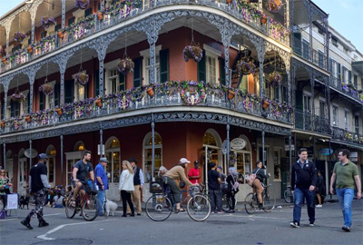 Picture shows a 3-story building with balconies along each floor, and people walking in the street.