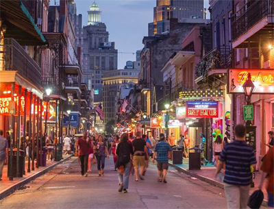 a narrow street lit up with the signs of many stores and restaurants is filled with people walking.